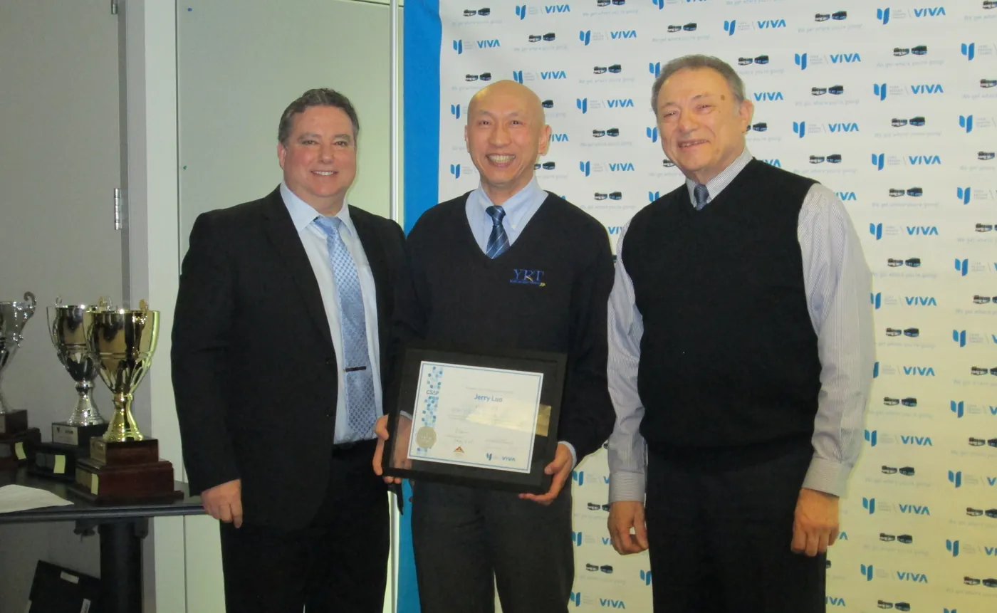 Three men in front of a York Region Transit backdrop, one holding a framed certificate, beside a table of trophies.