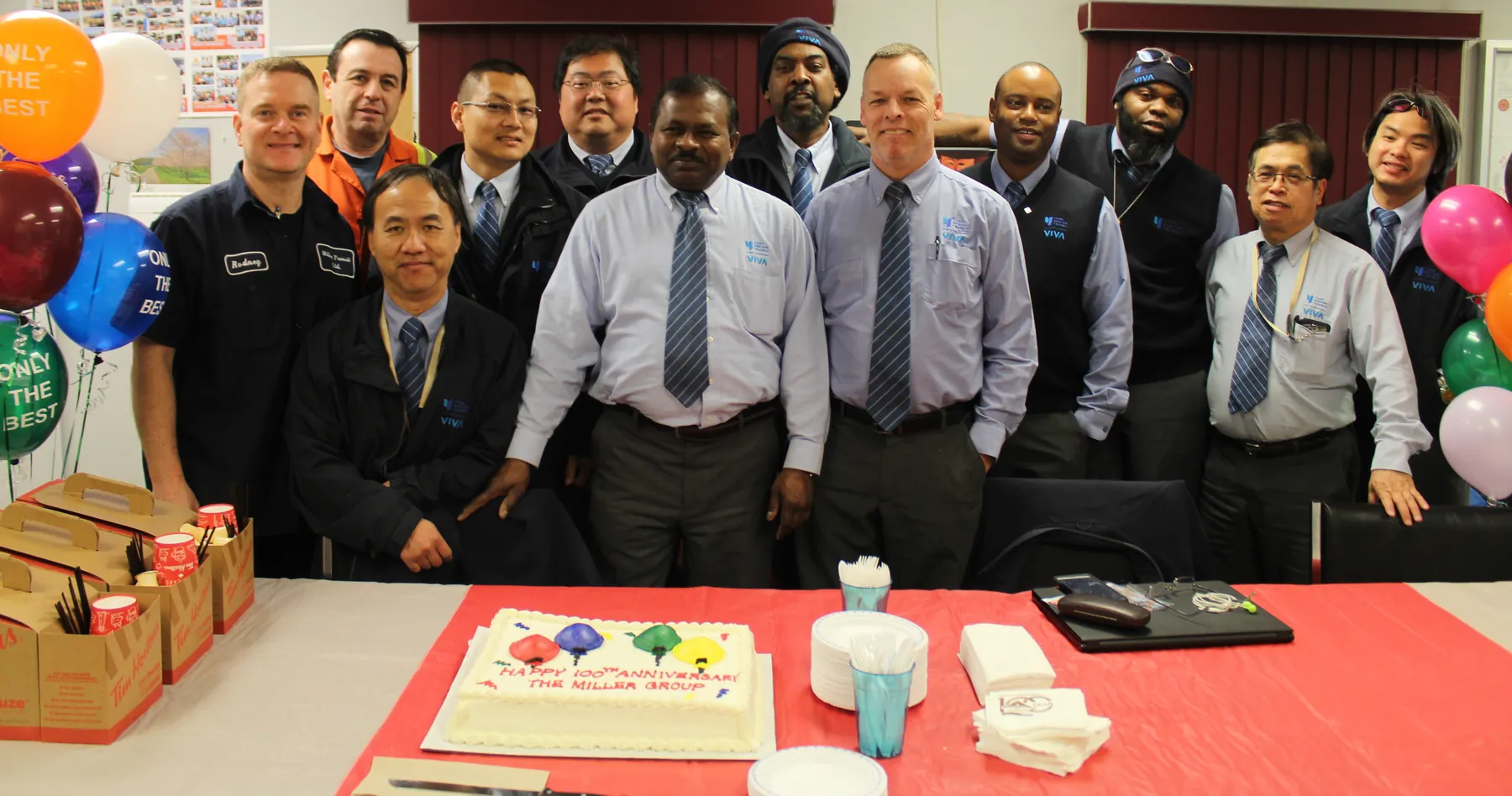 A group of Miller Transit employees in uniform gathered around a celebration cake.